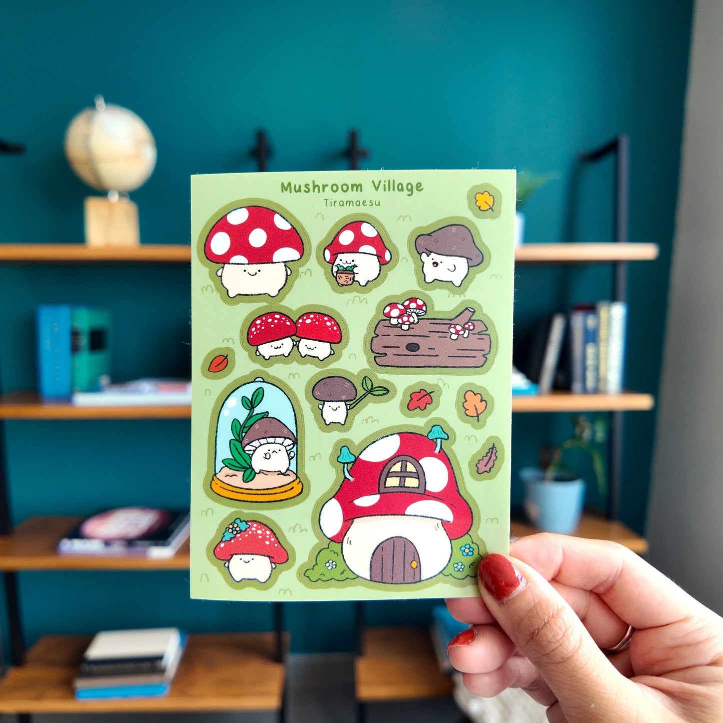 Sheet of mushroom-themed stickers held by a hand in front of a bookshelf.