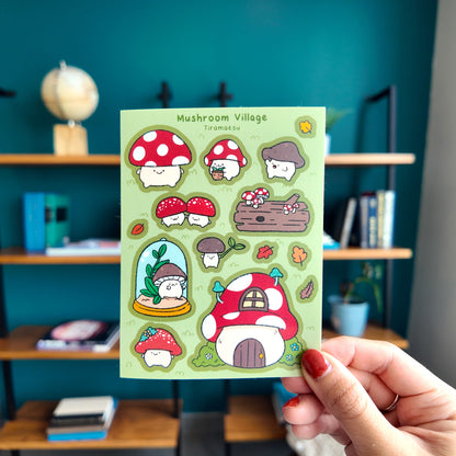 Sheet of mushroom-themed stickers held by a hand in front of a bookshelf.